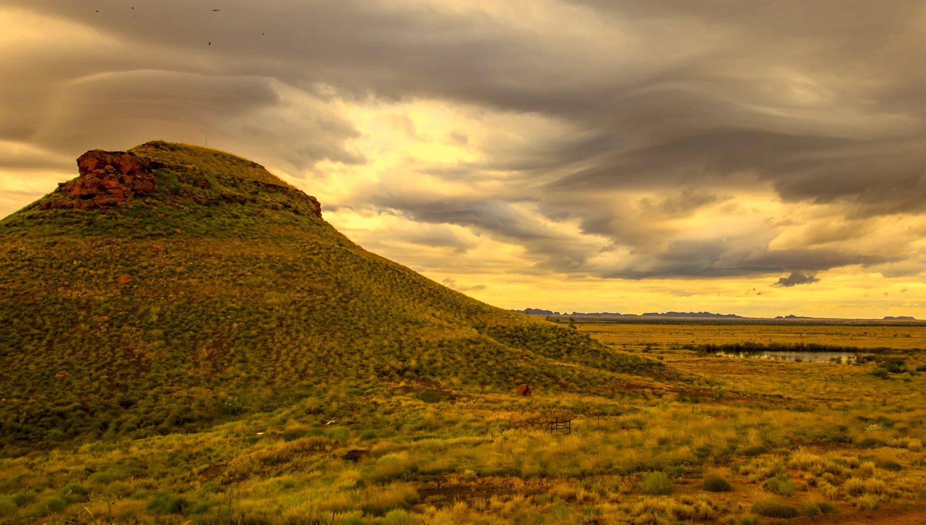 A weathered outback rise under a turning sky
